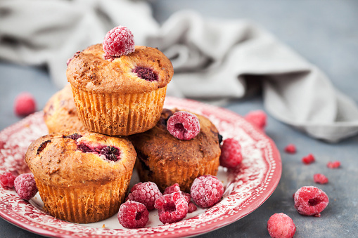 Stock photo showing elevated view of muffin baking tray with baked on dirt containing homemade blueberry muffins in brown paper cake cases on a mottled blue and brown surface. Home baking concept.