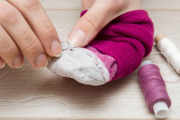 istock Hand with a needle and thread darning a sock. Sewing works. Handmade. Womanly hobby. 665731400