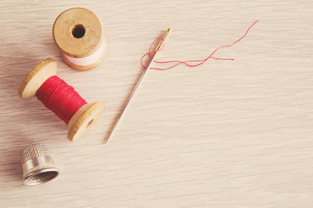 Thread, needle and iron thimble on the wooden table. Sewing works. Handmade.