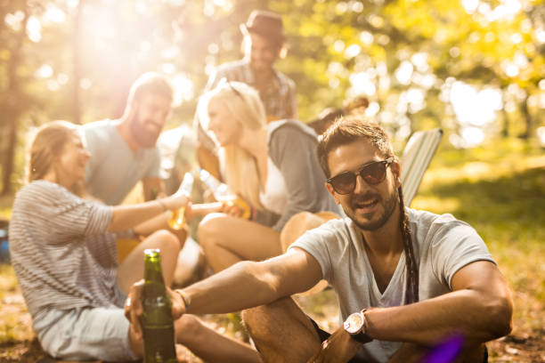 Young hipster man looking at camera while holding beer bottle and spending a day i nature with his friends.