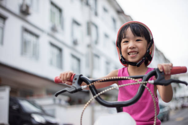 asian chinese little girl riding bicycle on tar road - helmet bicycle little girls child imagens e fotografias de stock