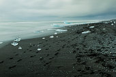 Blocks of ice and footprints on black sand beach