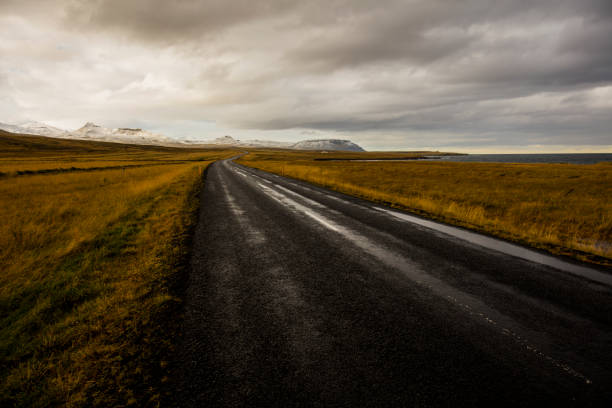 Empty road amidst volcanic landscape in Iceland. View of road leading towards mountains. Scenic view of nature against cloudy sky.