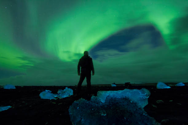istock Man watching Northern Lights at black sand beach 665761200
