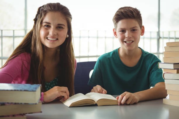 istock Smiling school kids reading books in library at school 665764396