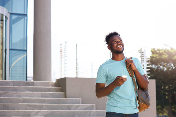 estudante universitário homem andando por escadas com bolsa e telefone inteligente - african ethnicity standing college student curly hair - fotografias e filmes do acervo