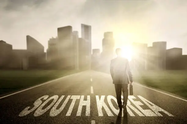 Young businessman carrying a suitcase and walking on the road with South Korea word