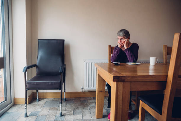 Senior Woman Sitting Beside an Empty Chair Senior woman sitting alone in her kitchen. She is looking at an empty chair beside her with a serious expression. widow stock pictures, royalty-free photos & images