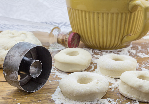 Close up photo of fresh donuts rolled out on floured wooden kitchen table and round donut cutter