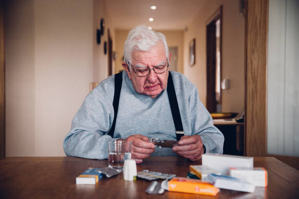 Elderly Man with all his Medication Elderly man sitting at home at a table with his head resting on his hand. Looking troubled he holds a packet of pills with other medication around him condition stock pictures, royalty-free photos & images