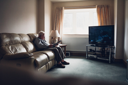 Senior man sitting alone at home. Sitting in his living room with a newspaper and holding a pen in his hands.