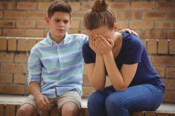 istock Schoolboy consoling her sad friend on steps in campus 665819994