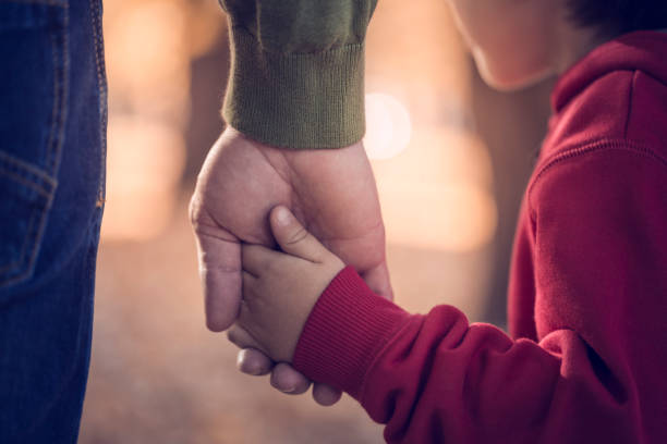 Father and son holding hands in park stock photo