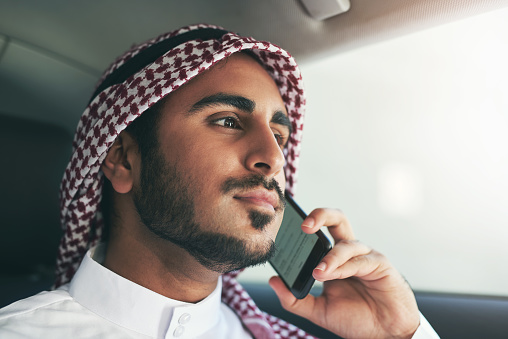 Shot of a young muslim businessman using his phone while traveling in a car