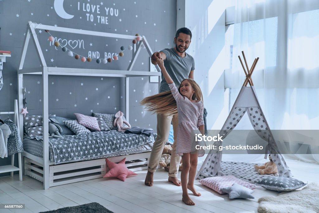 Going crazy together. Full length of father and daughter holding hands and smiling while dancing in bedroom Child Stock Photo