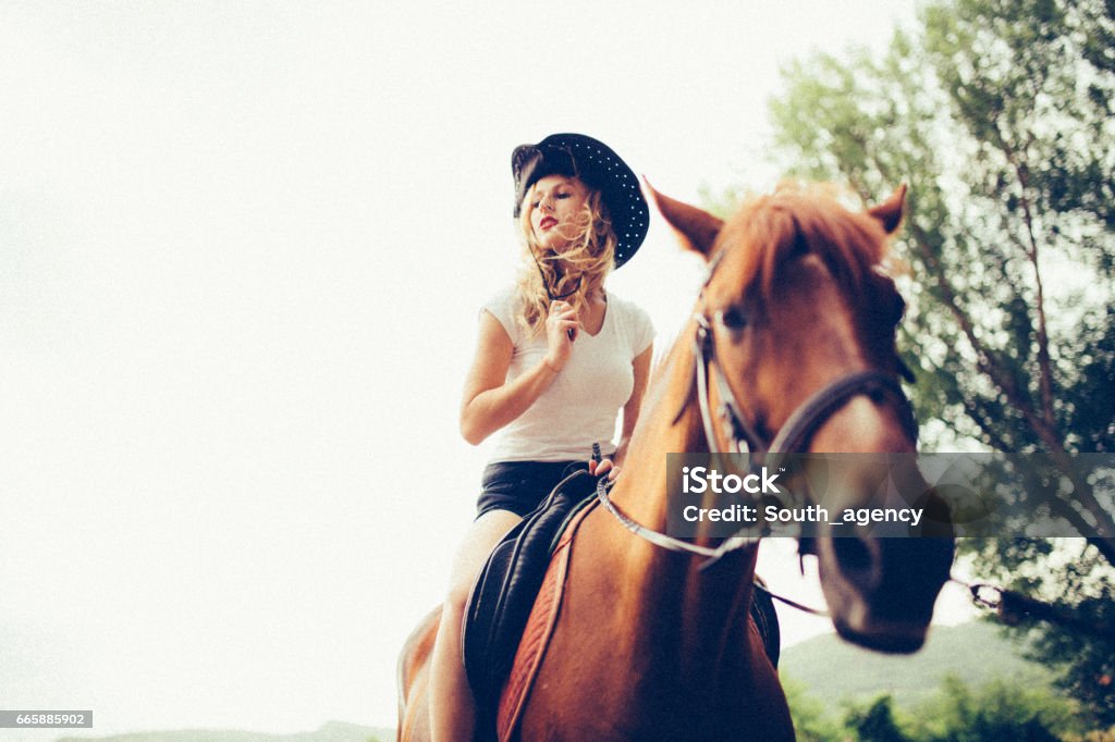 Cowgirl riding a horse Young curly blonde woman and her horse, enjoying the summertime away from the city. Adult Stock Photo