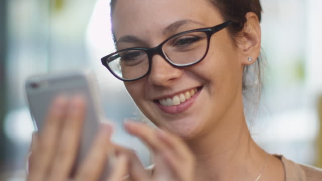 Caucasian Ethnicity Smiling Young Woman using Mobile Phone at Cozy Coffee Shop.