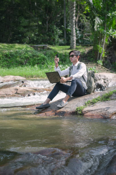 istock Businessman with backpack and laptop and phone at  waterfall  the forest. 665893892