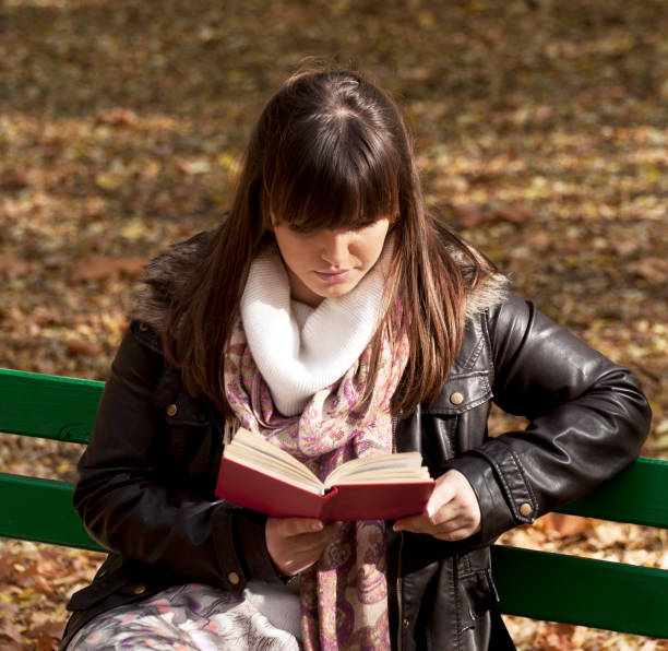 istock Beautiful woman sitting on a park bench and reading a book 665900082