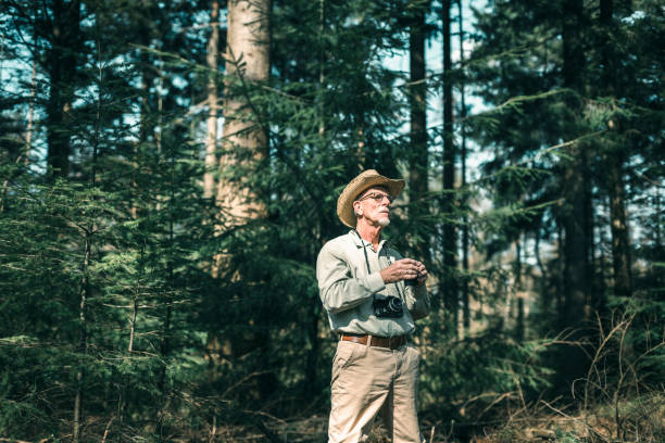 istock Senior man with binocular in pine forest wearing hat. 665907190