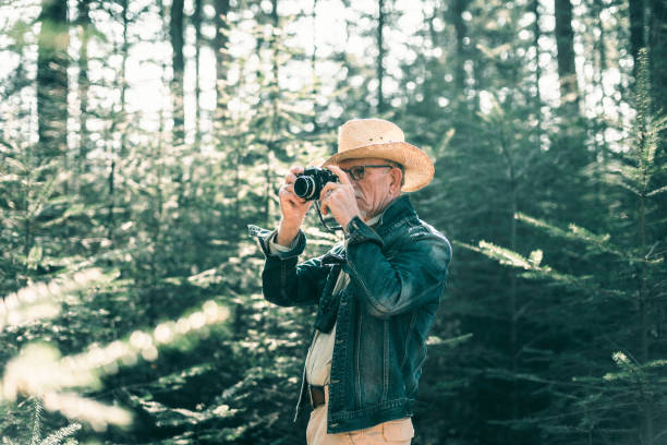 istock Senior man with hat photographing in pine forest. 665907294