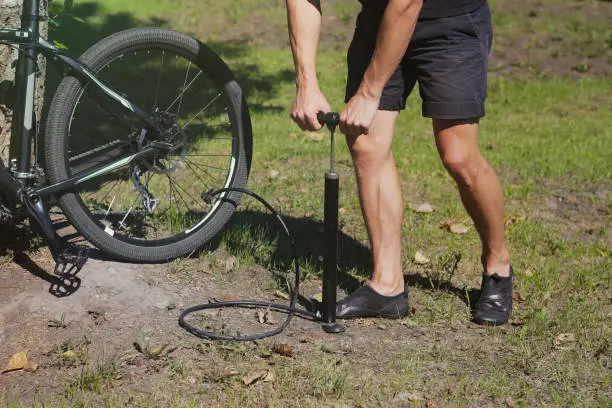 Inflating the tire of a bicycle. Cyclist repairs bike in forest. Bicyclist pumping air into the wheel. Biker uses a bicycle pump. Pumping air into an empty wheel of bike.
