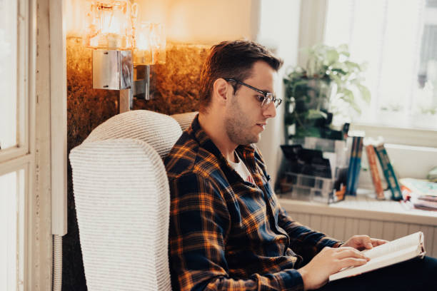 istock Charming young adult is wearing glasses while he's reading a book 665946104