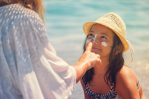 Young mother applying suntan lotion on daughter's face at the beach
