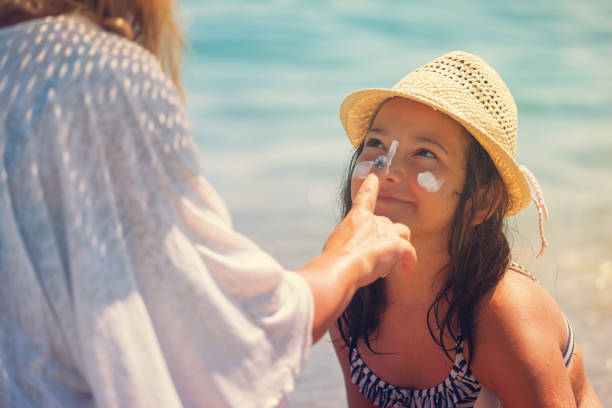 młoda matka stosująca balsam do opalania na twarzy córki - enjoyment people beach sun protection zdjęcia i obrazy z banku zdjęć