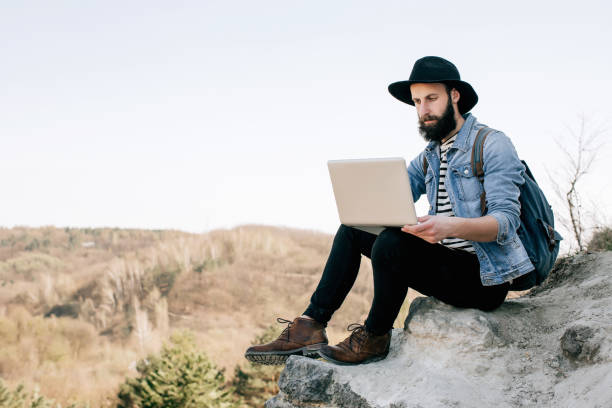 istock handsome bearded man freelancer working on a laptop outdoors in mountains. Freelance concept 665951502
