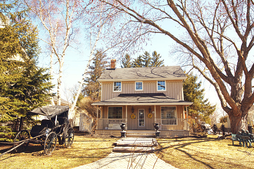Kleinburg, Ontario, Canada - April 2, 2017: A traditional old-fashioned Canadian house with a vintage carriage and a huge trees on the front yard on a beautiful April sunny day in Kleinburg Village (Vaughan), Ontario, Canada
