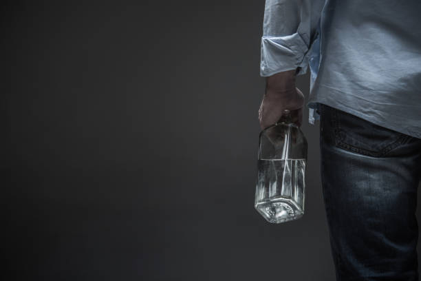 Photo of male back holding bottle in hand It is a problem. Close up of stylish man wearing casual clothes keeping bottle with beverage in hand while standing isolated on grey background alcohol abuse photos stock pictures, royalty-free photos & images