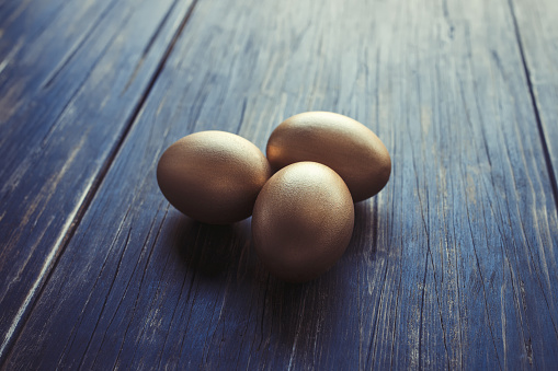 Three golden eggs on an old rustic wooden table