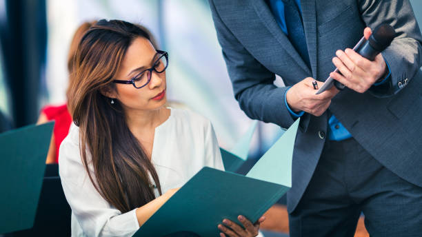 Business people attending a presentation A young asian businesswoman at a business presentation in the board room, showing a document to the presenter presentation folder stock pictures, royalty-free photos & images