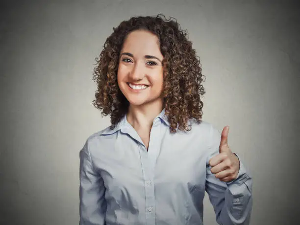 Closeup portrait young, curly brown hair woman student being excited giving showing thumbs up hand gesture isolated grey background. Positive human emotion face expression feeling sign symbol attitude