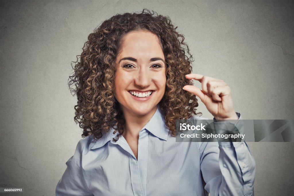 Happy smiling young woman Closeup portrait, funny young curly brown hair woman showing small amount gesture with hand fingers isolated grey background. Human emotion facial expression feelings, body language, signs, symbols Abundance Stock Photo