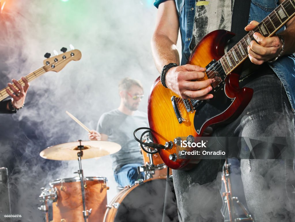 Rock band performs on stage. Guitarist, bass guitar and drums. Rock band performs on stage. Guitarist, bass guitar and drums. Guitarist in the foreground. Close-up. Rock Music Stock Photo