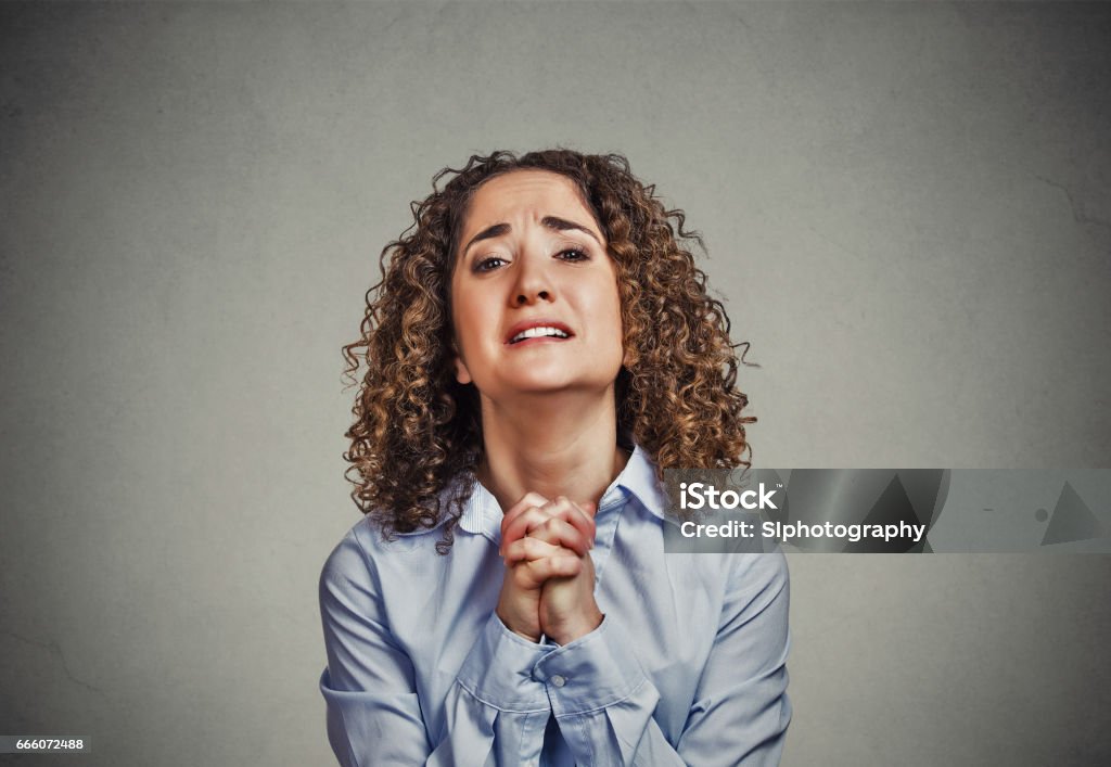 young woman gesturing with clasped hands, pretty please Closeup portrait young woman gesturing with clasped hands, pretty please with sugar on top, isolated gray background. Human emotion facial expression feeling, signs symbols, body language Pleading Stock Photo