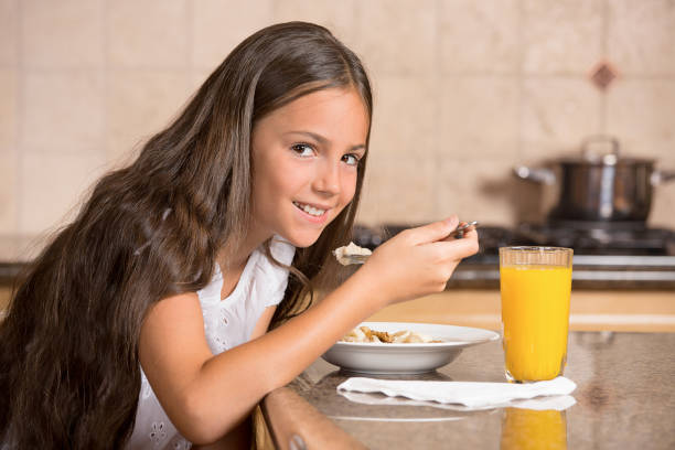 menina bonito do adolescente que come o cereal com leite que bebe o sumo de laranja para o pequeno almoço na cozinha - healthy eating snack child domestic kitchen - fotografias e filmes do acervo