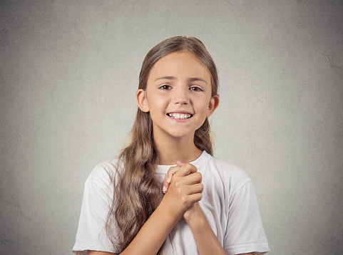 Closeup portrait teenager girl gesturing with clasped hands, pretty please with sugar on top, isolated grey wall background. Human emotions, facial expressions, feelings, signs symbols, body language