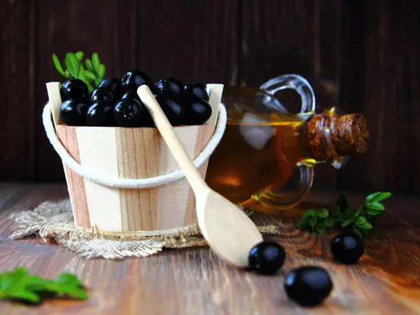 olives in a wooden bucket with a spoon and olive oil