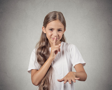 Secret. Closeup portrait teenager girl placing finger on lips mouth with shhh sign symbol, isolated grey wall background. Human emotion facial expression feelings, body language, attitude
