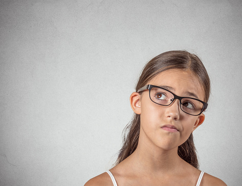 Closeup portrait skeptical young girl looking up, suspicious, skepticism on face, disapproval isolated grey wall background. Negative human emotions, facial expressions, feeling attitude body language