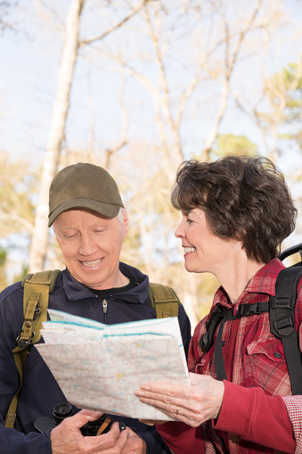 Active senior adult couple hiking through a wooded forest area.  They wear backpacks and are enjoying nature.