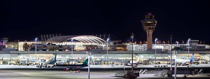 Franz-Josef-Strauss Munich airport with control tower, four passenger airplanes standing at the gates, apron area, long exposure with tripod, horizontally stitched composition.

