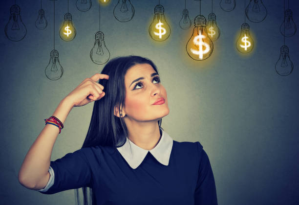 istock thinking young woman looking up at dollar idea light bulbs 666119966