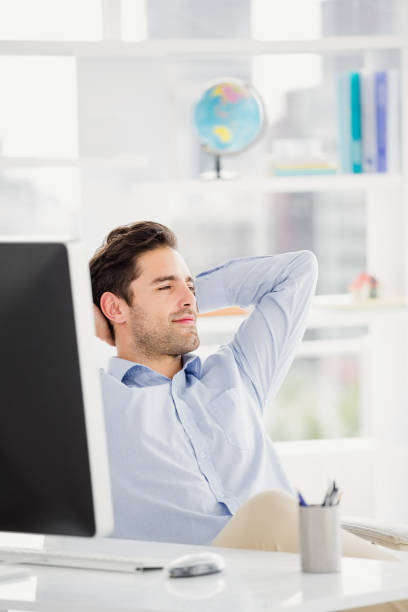 Successful businessman sitting daydreaming at the office with a pleased smile sitting relaxing in his chair with his hands clasped behind his head
