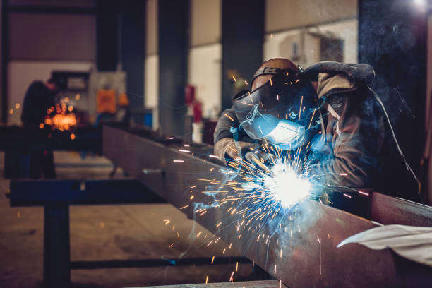 Industrial Welder With Torch Industrial Welder With Torch and Protective Helmet in big hall welding metal profiles manufacturing occupation photos stock pictures, royalty-free photos & images