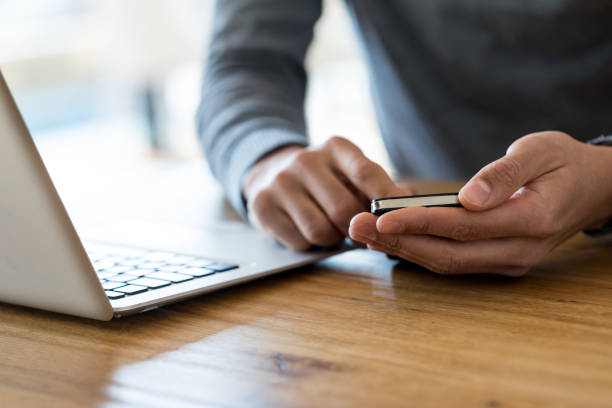 der mann hält handy am arbeitsplatz zugeschnitten - desk men sitting computer stock-fotos und bilder