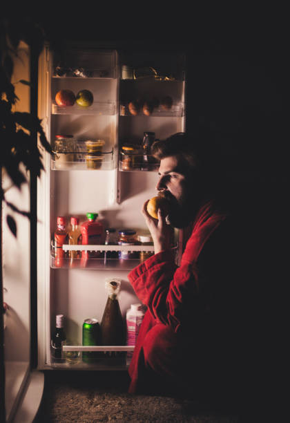 istock Man eating apple late night in front of the refrigerator 666188102